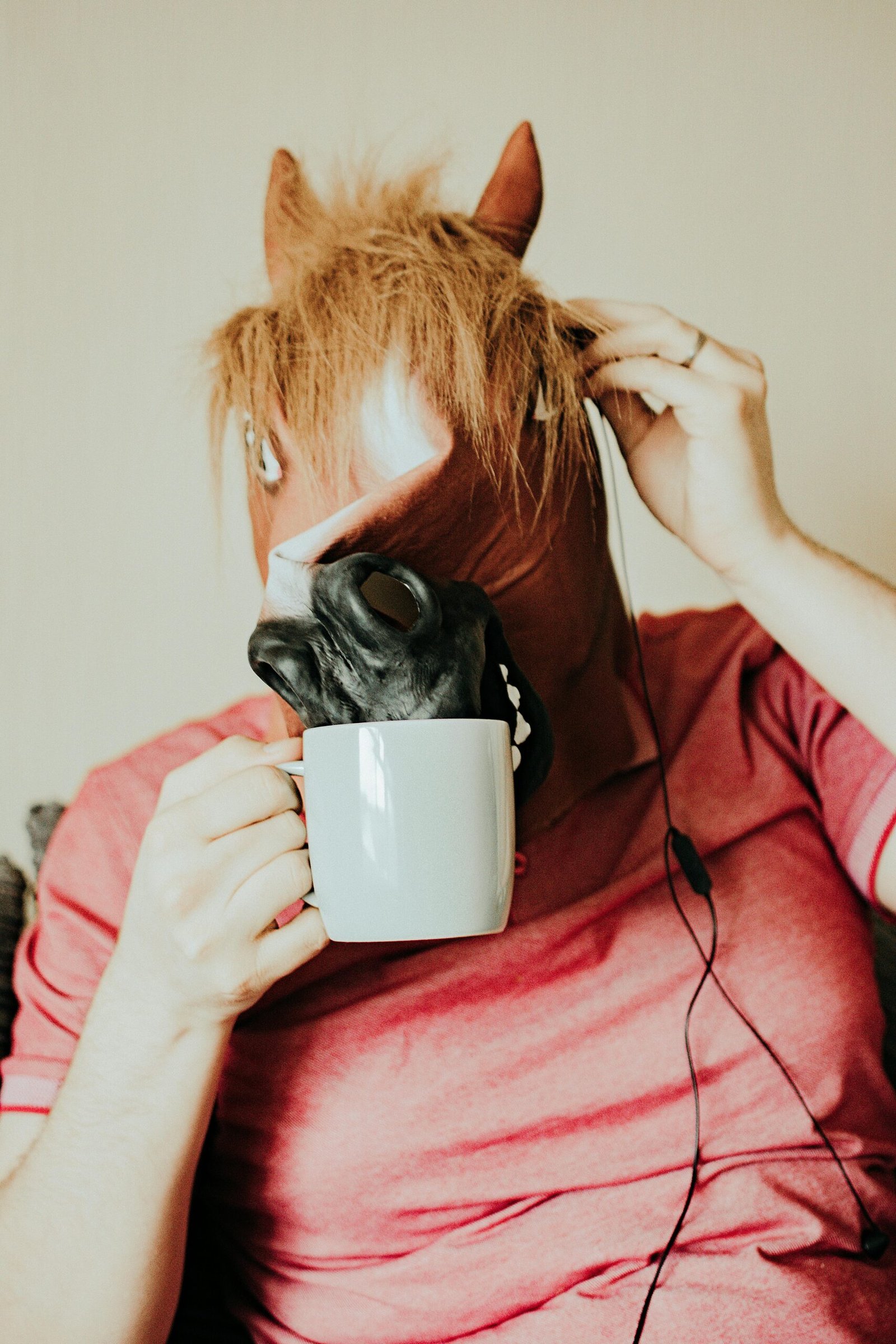 A humorous image of a person wearing a horse mask while drinking from a mug indoors.